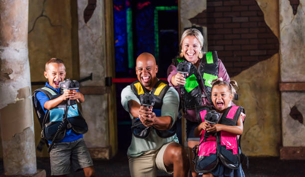 Interracial family with two children playing laser tag An interracial family having fun together at an amusement arcade playing laser tag. The African-American father and Caucasian mother are in their 30s. The two mixed race children are 9 and 5 years old. They are laughing and shouting, aiming their lasers toward the camera. playing tag stock pictures, royalty-free photos & images