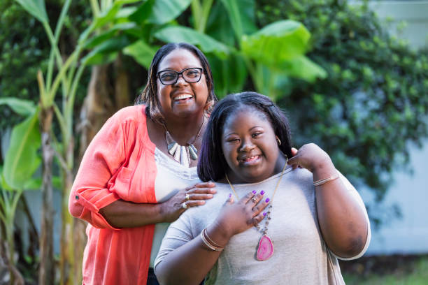 African-American grandmother and teen girl with downs An African-American woman in her 50s standing with her teenage granddaughter, 16 years old, who has down syndrome. They are outdoors, in the back yard of their home, smiling at the camera. disabled adult stock pictures, royalty-free photos & images