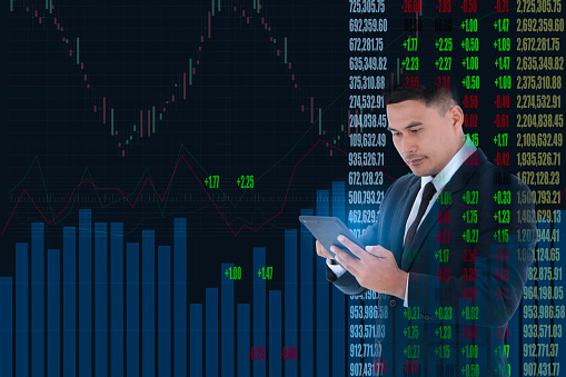 Double exposure Asian Businessman looking at tablet screen stock market. Financier are checking stock exchange data on digital display of graphs and numbers. Concept investment finance analysis broker