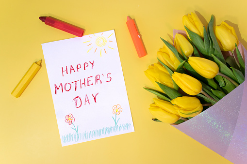 Greeting card for Mom on Mother's Day, colorful crayons and yellow tulips on yellow background. Child`s drawing with inscription \