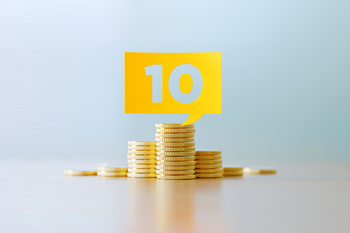 Number 10 written yellow speech bubble sitting over coins stacks before defocused background. Horizontal composition with copy space. Great use for budget concepts.