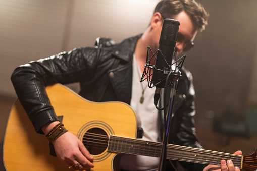 Male singer playing guitar in recording studio.