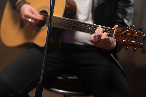 Midsection of male singer playing guitar in recording studio.