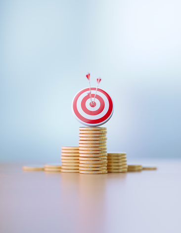Red dartboard and arrows sitting over coin stacks before defocused background. Vertical composition with copy space. Success and accuracy concept.