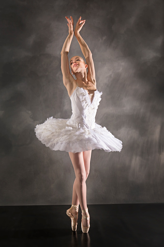 Beautiful young woman ballet dancer sitting in splits on a floor. She is posing with her head on her hand. The ballerina is smiling looking at the camera. Studio shooting on background of copper color grunge texture wall