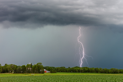 Thunderstorm and lightning bolt strike with rain and dark storm clouds over a field in Minnesota.