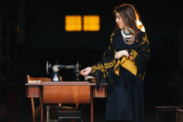 Hands of happy young seamstress by retro sewing machine making dress