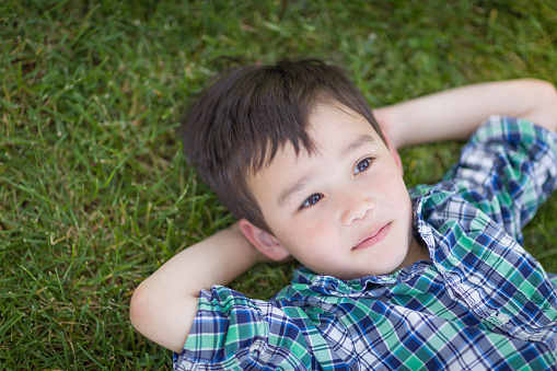 Thoughtful Mixed Race Chinese and Caucasian Young Boy Relaxing On His Back Outside On The Grass.
