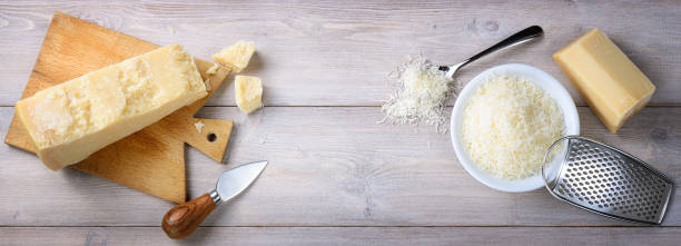 Parmesan pieces and grated on wooden background, top view, space for text. Parmesan aged 30 months with knife, cutting board and grater on wooden table. Flat lay. grated stock pictures, royalty-free photos & images