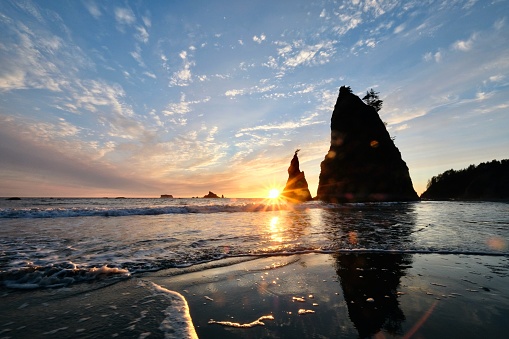 Sea Stack rocks silhouettes reflections in water at sunset.