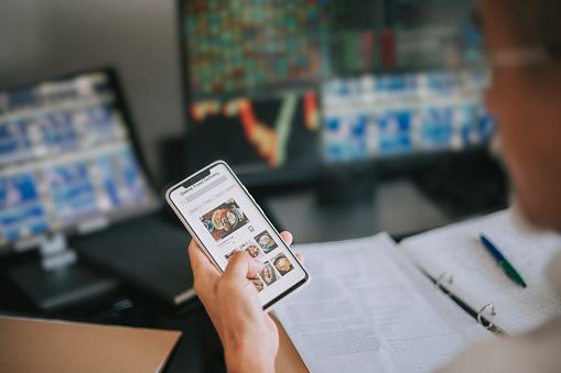 Online food delivery mobile app shown on smart phone screen hold by asian man hands in front of desktop pc