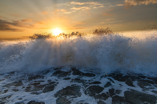 A Wave Is Crashing On Shore As The Sun Sets On the Ocean Horizon