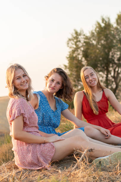 istock Three girls sit in a field while smiling at the camera 1307502725