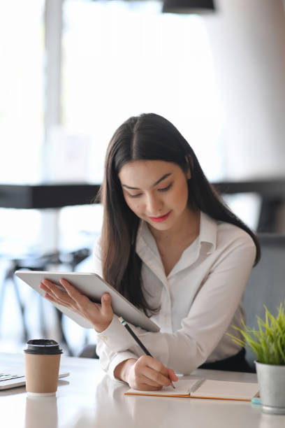 istock Portrait of young businesswoman using digital tablet and making note on note book. 1307506944
