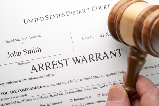 Arrest Warrant document with gavel and hand