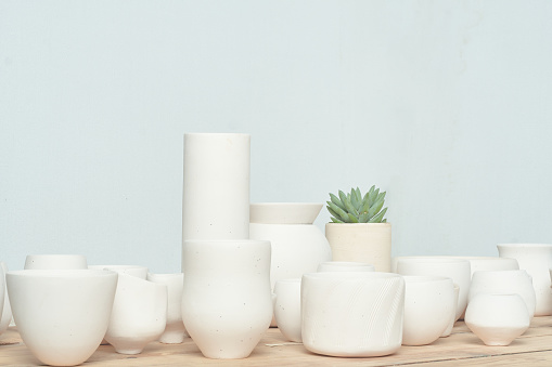 All kinds of handmade white clayware, randomly combined and placed on the unpainted wooden table. The light background environment is very bright, fresh, elegant and energetic. There is also a small green succulent plant for decoration.