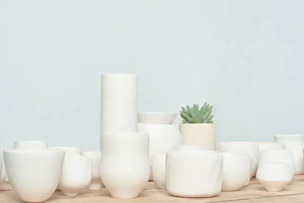 All kinds of handmade white clayware, randomly combined and placed on the unpainted wooden table. The light background environment is very bright, fresh, elegant and energetic. There is also a small green succulent plant for decoration.