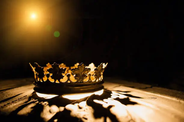 Photo of The crown on a black background is illuminated by a golden beam. Low-key image of a beautiful queen / royal crown Vintage is filtered. Fantasy of the medieval period. Battle for the Throne.