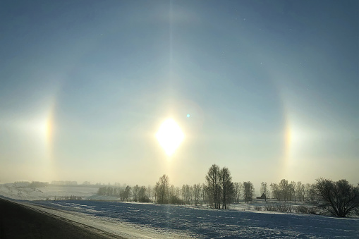 Halo effect over the frozen winter forest, view from the country road. Magical unbelievable nature phenomenon