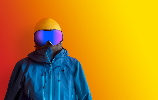 Front portrait of a man in skiing / snowboarding clothes over a contrast background with copy space for additional content.