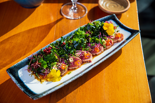 Tuna tataki slices served with edible seaweed, sesame, caviar and garlic chips on rectangular plate
