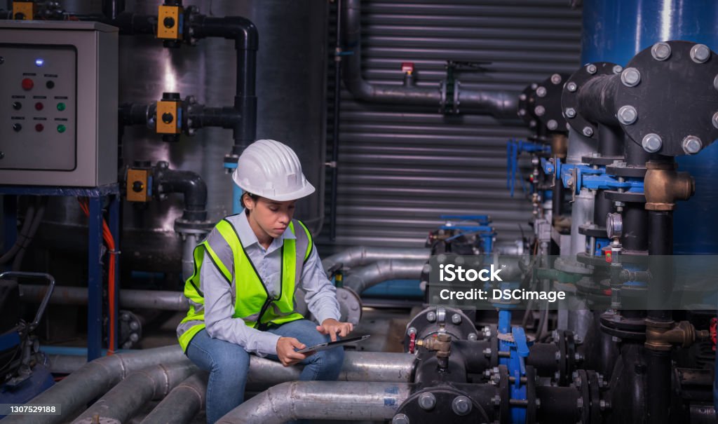 Industry engineer worker wearing safety uniform under checking the industry cooling tower air conditioner is water cooling tower air chiller HVAC of large industrial building to control air system. Cooling Tower Stock Photo