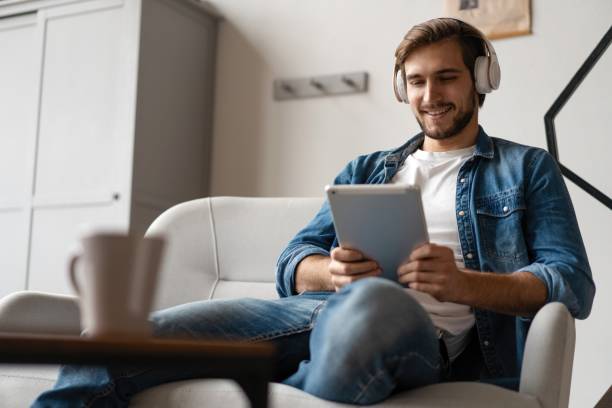 istock Cheerful young man holding digital tablet and looking relaxed while lying on the couch at home 1307529806