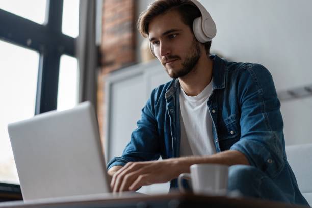 istock Man Using Laptop Wearing Headphones Relaxing Sitting On Sofa At Home. 1307529812