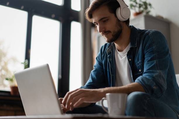 istock Man Using Laptop Wearing Headphones Relaxing Sitting On Sofa At Home. 1307529823