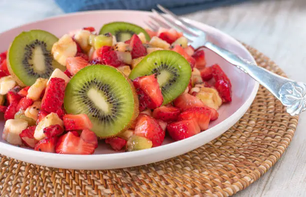 homemade fresh fruit salad with a fruit mix of strawberries, bananas and kiwis cut into pieces and slices and served on a plate
