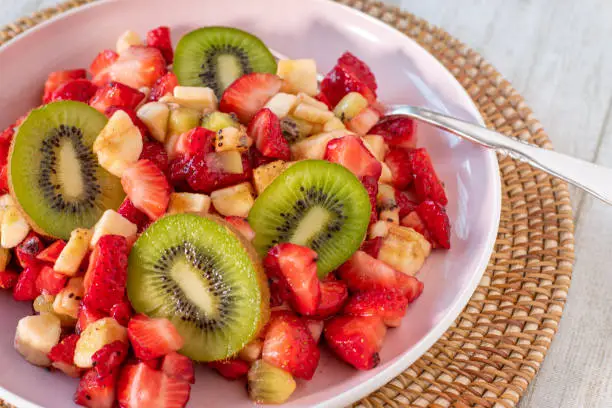 A plate of fresh fruit salad with strawberries, kiwis and bananas served isolated on a plate from above