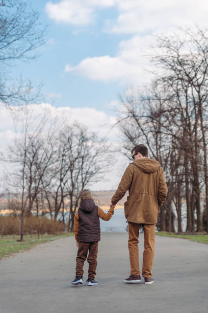 istock father with son walking by park holding hands 1307534785