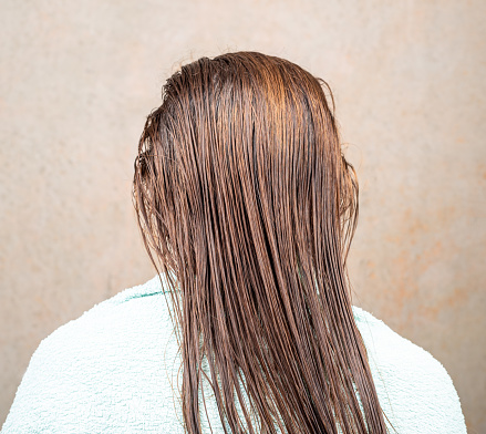 A woman sits with her back to the camera with her wet hair combed. Hair care.