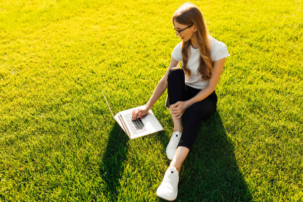 istock Young woman sits in a park on green grass, using laptop, summer sunny day 1307538432