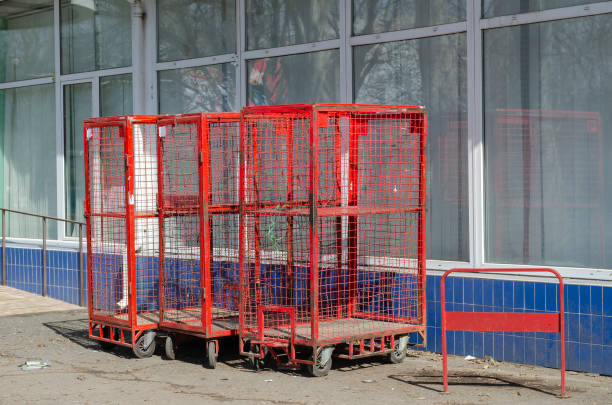 Red cages on wheels outside the building. Storage cages against a glass wall. Logistics and warehouse storage. Sunny day. No people.