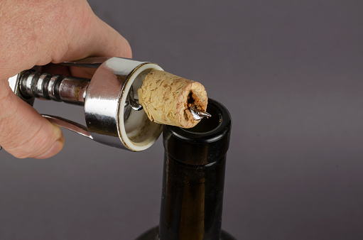 Wine bottle, hand with a corkscrew and a broken cork on a gray background. A man's hand holds a corkscrew with a broken wine stopper.
