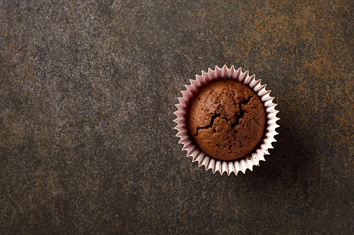 Chocolate homemade cupcake with paper form for baking on wooden background, copy space, top view, close up