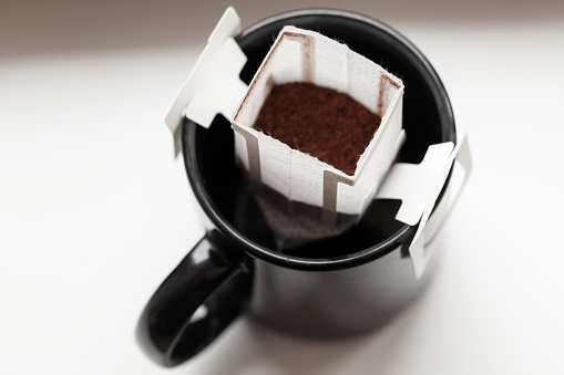 Drip coffee bag is in a black cup ready for brew, closeup photo with selective focus