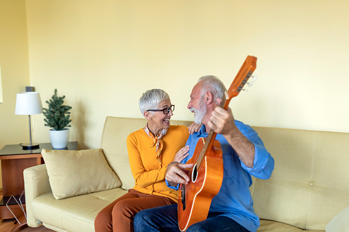 A Cheerful Couple is Relaxing and Enjoying the Sounds of Guitar at Home. Happy Husband is Sharing Positive Moments with his Beautiful Wife in the Living Room of Comfortable Apartment.