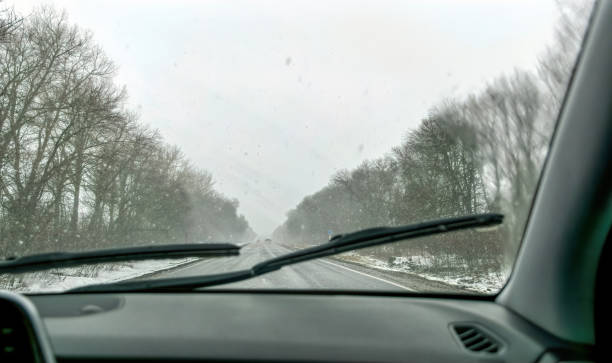 istock Car wipers wiping the windshield. Winter highway during snowfall 1307547035