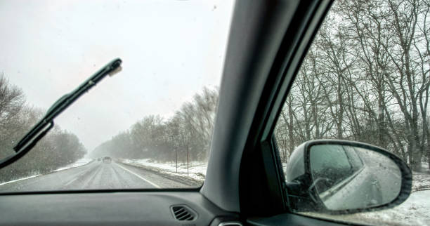 car wipers wiping the windshield. winter highway during snowfall - snow driving side view mirror rain imagens e fotografias de stock