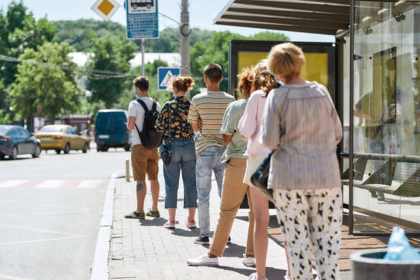 Full length shot of people wearing masks waiting, standing in line, keeping social distance at bus stop. Coronavirus, pandemic concept Full length shot of people wearing masks waiting, standing in line, keeping social distance at bus stop. Coronavirus, pandemic concept. Selective focus on guy in the queue. Horizontal shot bus photos stock pictures, royalty-free photos & images