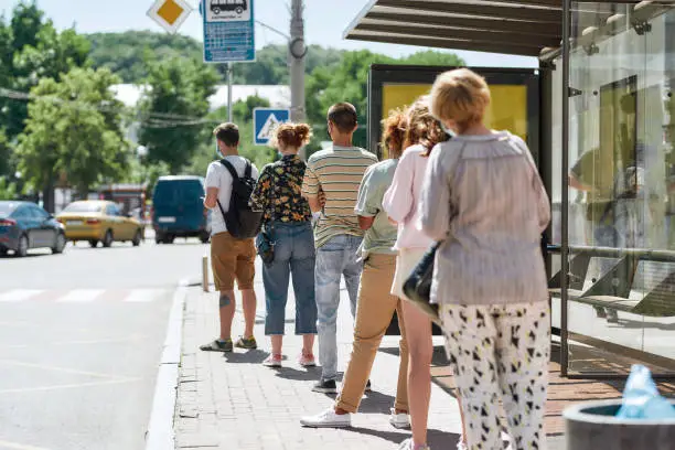 Photo of Full length shot of people wearing masks waiting, standing in line, keeping social distance at bus stop. Coronavirus, pandemic concept