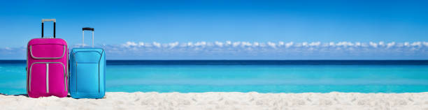 istock Two suitcases on sandy tropical seashore. Vacation on the beach. Travel concept. Long header 1307549788