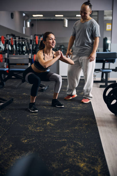 istock Young cheerful woman doing squats with her trainer 1307550322