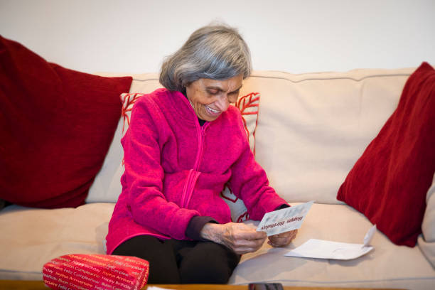 Senior Indian woman opening gift and birthday card, UK Elderly senior Indian woman opening a birthday card and gift or present. Ethnic Asian lady at home in England, UK senior birthday card stock pictures, royalty-free photos & images