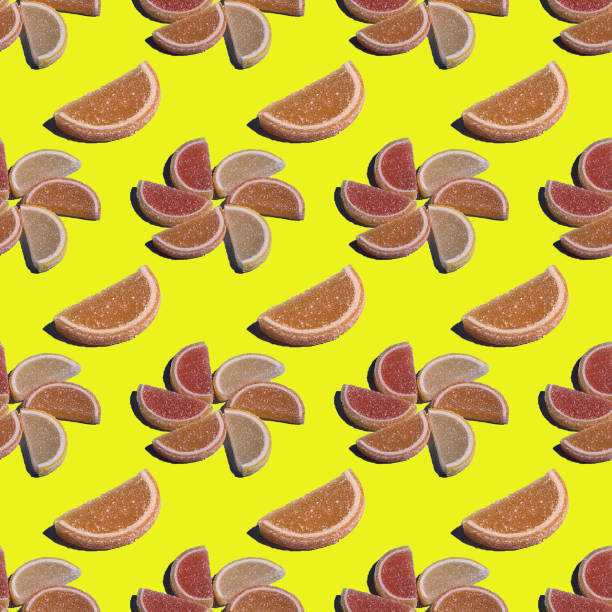 A decorative seamless candy pattern of marmalade in the form of citrus slices is laid out in the form of flowers on a yellow background. Jelly sweet candies. Top view.