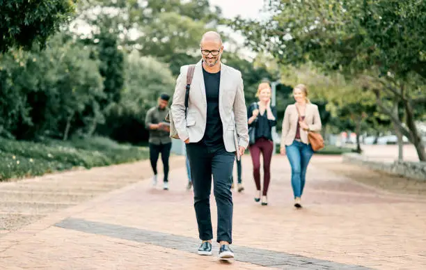 Shot of a confident mature businessman walking through the city with a young team behind him