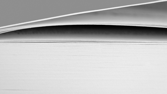 Black and white macro side view close-up of white pages in a thick book and its cover, one can clearly see that (only) the first few pages have been read so far