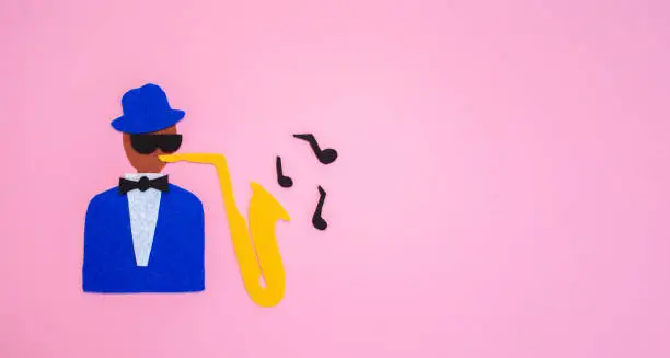 Photo of World Jazz Day. Silhouette of a musician with a saxophone on a pink background, cutted out of felt. Flat lay. Banner. Copy space